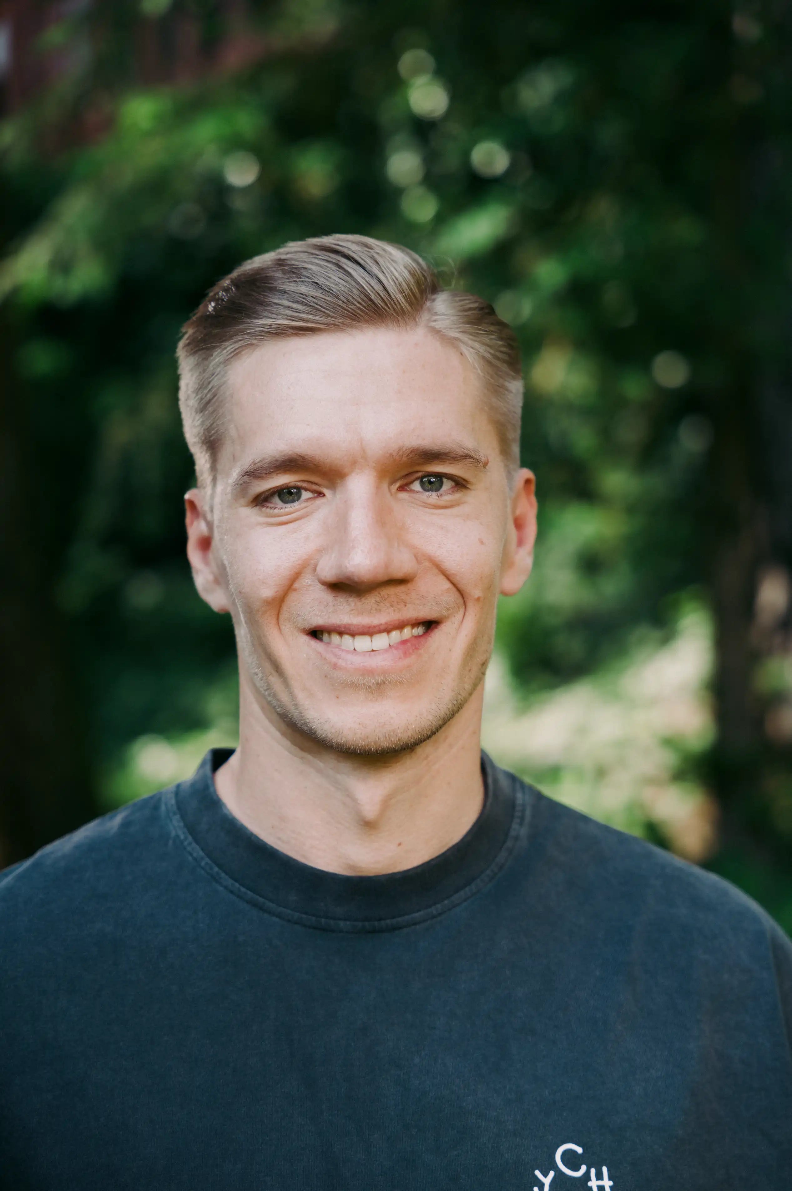 Nahaufnahme eines lächelnden Mannes mit kurzen blonden Haaren im dunkelgrauen Chumy-Shirt. Das Wiener Team hinter der nachhaltigen Ausdauersport-Nahrung. 