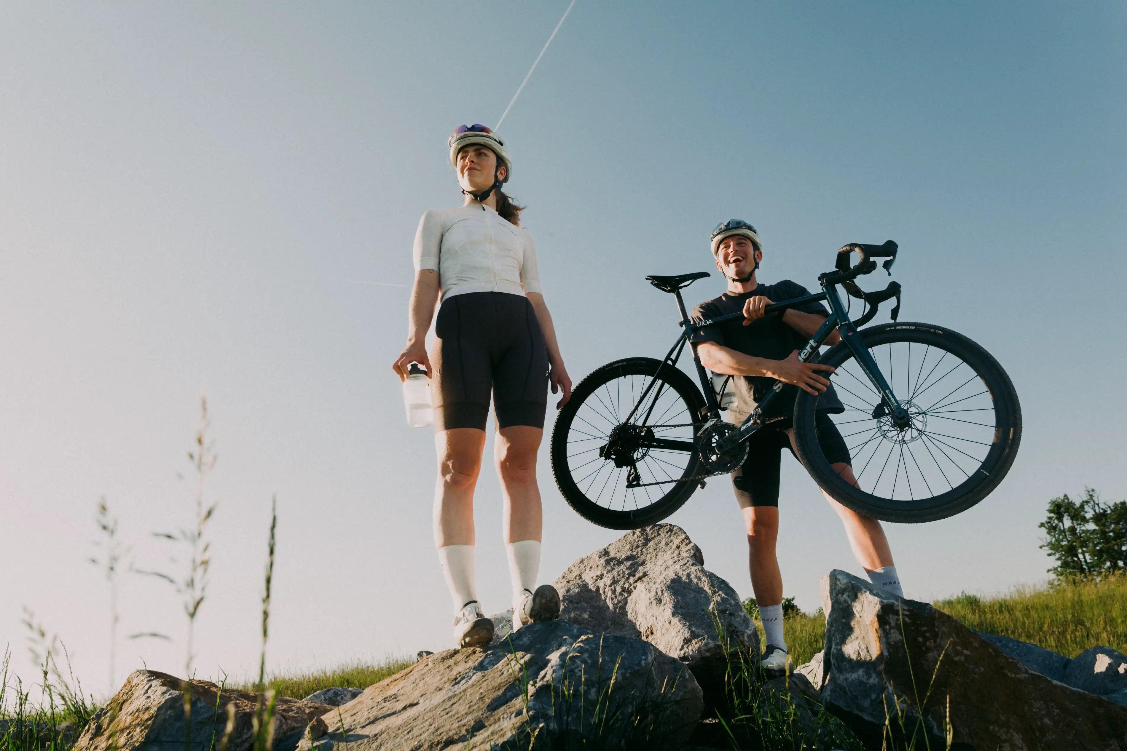 Ein Radfahrer und eine radfahrerin stehen im Sonnenuntergang und genießen die Szene. Sie trinken Elektrolyte und Kohlenhydrate. 